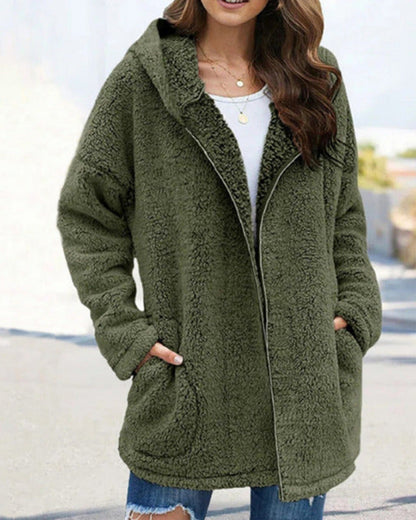 Frau in olivgrünem Teddy-Mantel mit Kapuze, lässig über weißem Shirt und Jeans getragen. Modetrend Herbst/Winter, gemütlicher Streetstyle-Look.