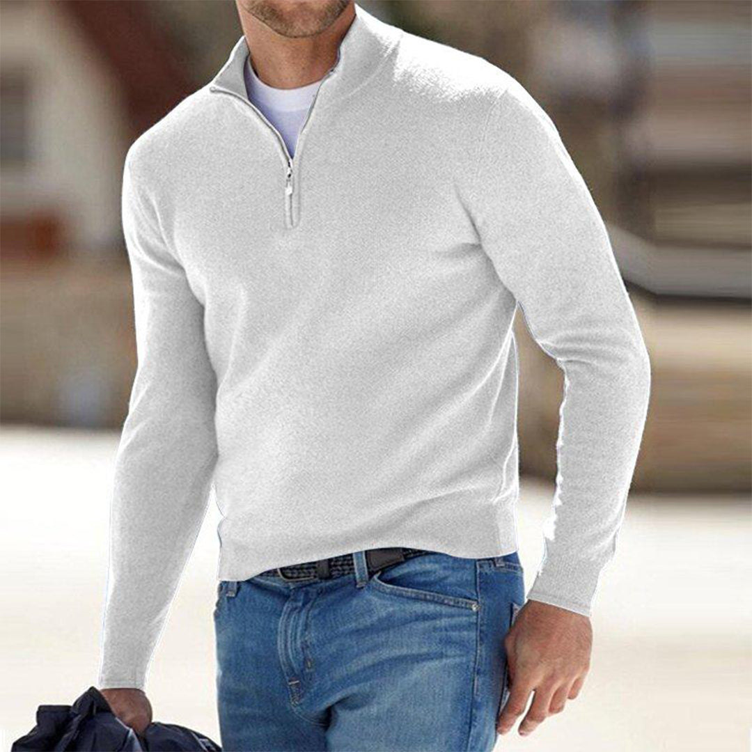 Mann in weißem Pullover mit Reißverschluss und blauer Jeans, hält Jacke. Modischer Freizeitlook, ideal für kühle Tage. Herrenmode, stilvoll und bequem.