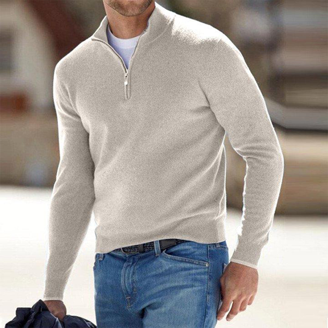 Mann in beigem Pullover mit Reißverschluss und blauer Jeans, hält Jacke. Modetrend Herrenmode, lässiger Look, stilvoller Freizeitstil.