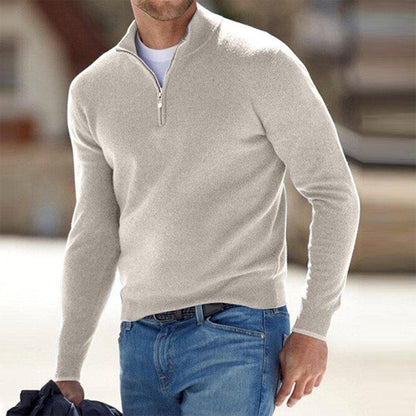 Mann in beigem Pullover mit Reißverschluss und blauer Jeans, hält Jacke. Modetrend Herrenmode, lässiger Look, stilvoller Freizeitstil.