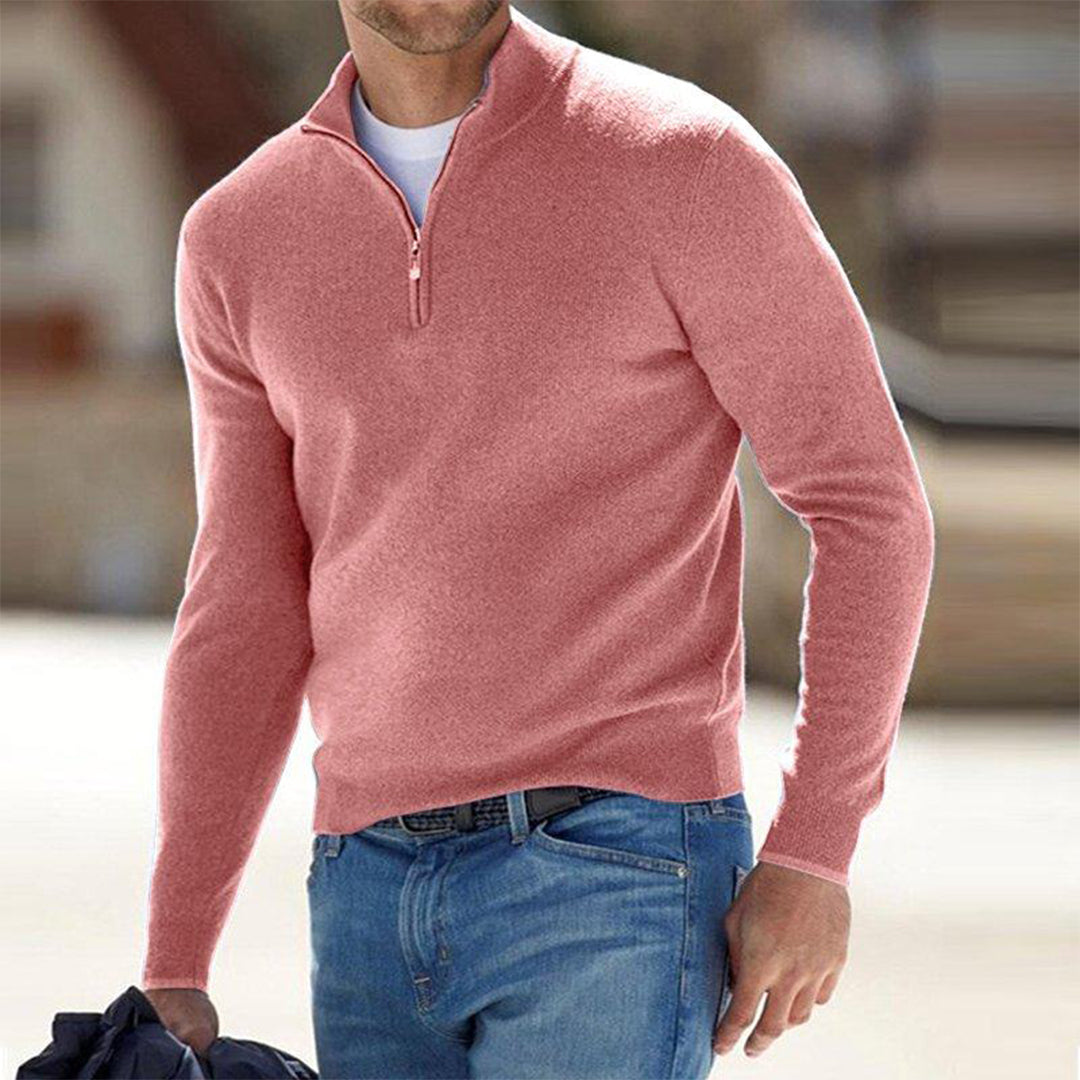Mann in rosa Pullover mit Reißverschluss und blauer Jeans, hält Jacke. Modischer Freizeitlook, ideal für Herbstmode und Herrenbekleidung.