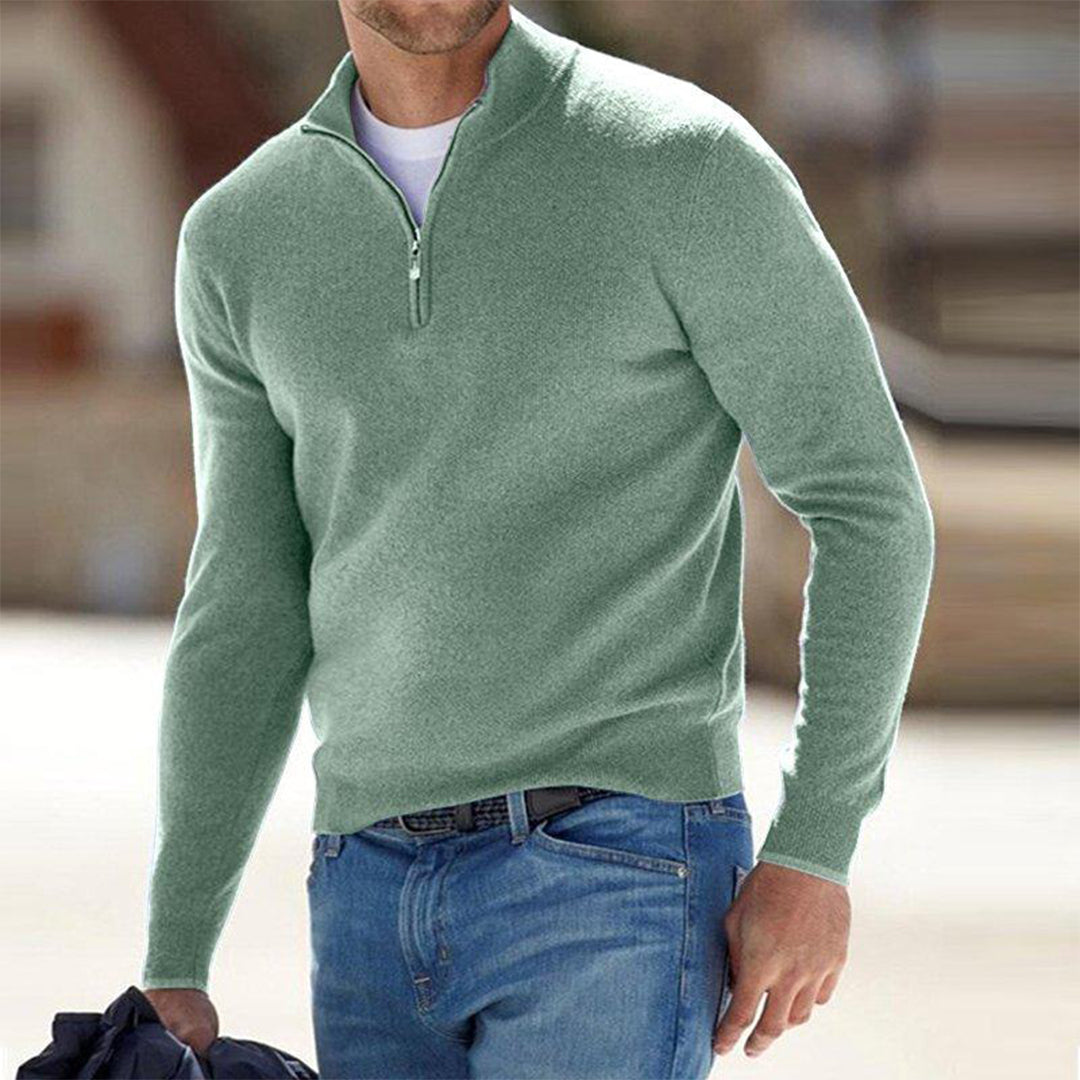 Mann in hellgrünem Pullover mit Reißverschluss, lässig gekleidet in blauer Jeans, hält Jacke. Mode, Herrenbekleidung, Freizeitlook.