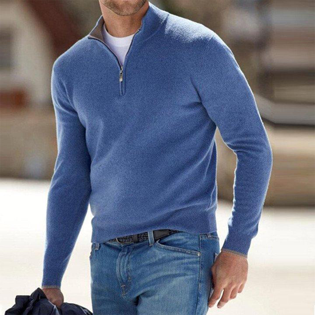 Mann in blauem Pullover mit Reißverschluss und blauer Jeans, hält Jacke. Modischer Freizeitlook, ideal für kühle Tage. Herrenmode, stilvoll und bequem.