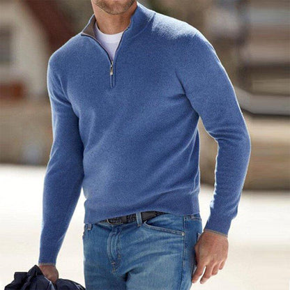 Mann in blauem Pullover mit Reißverschluss und blauer Jeans, hält Jacke. Modischer Freizeitlook, ideal für kühle Tage. Herrenmode, stilvoll und bequem.