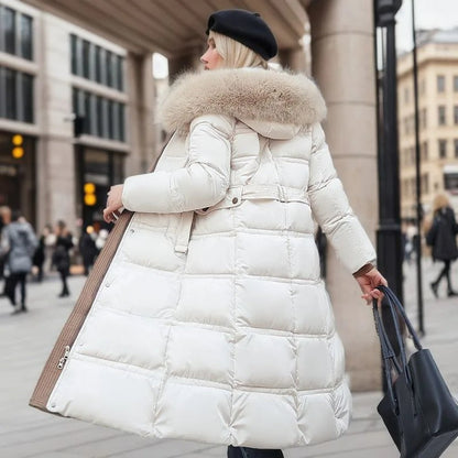Frau in weißem Daunenmantel mit Fellkragen und schwarzem Barett, hält eine Tasche, geht durch eine urbane Umgebung. Wintermode, stilvoll, elegant.