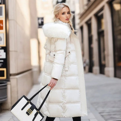 Blonde Frau in weißem Daunenmantel mit Fellkapuze, hält stilvolle Handtasche, steht auf städtischer Straße. Wintermode, eleganter Look, Stadtbummel.