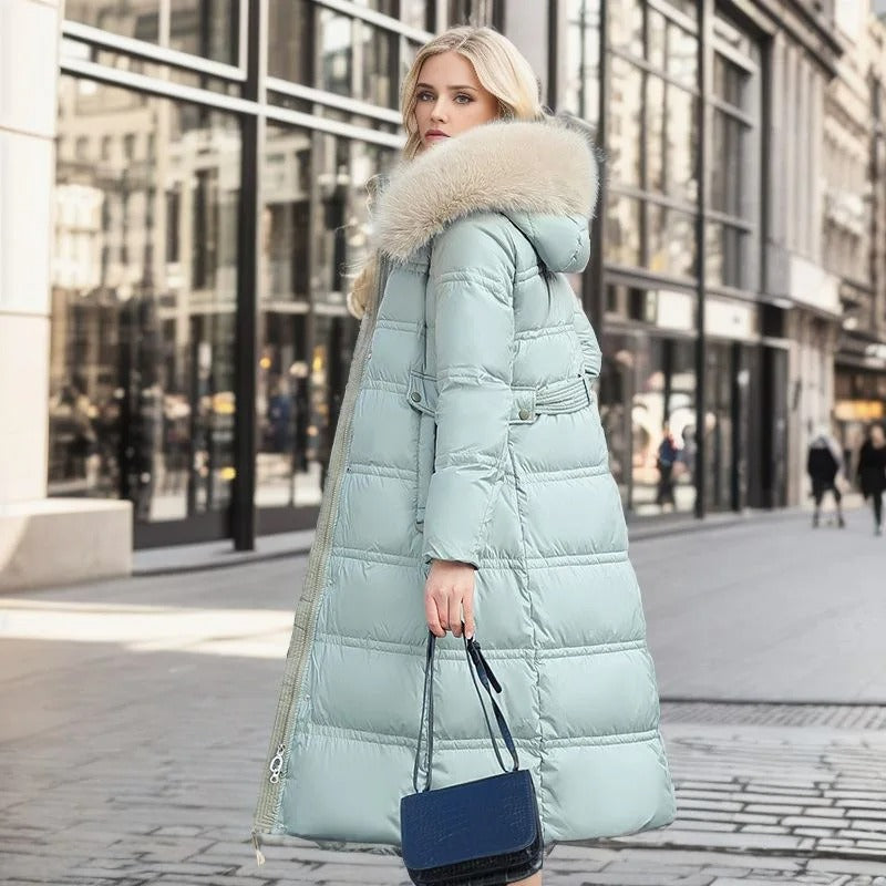 Frau in hellblauem Daunenmantel mit Fellkapuze, hält eine blaue Handtasche, steht auf städtischer Straße. Wintermode, stilvoll, elegant.