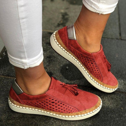 Rote Damen-Sneaker aus Wildleder mit Quasten und perforiertem Design, getragen zu weißen Hosen. Bequeme Freizeitschuhe für den Alltag.