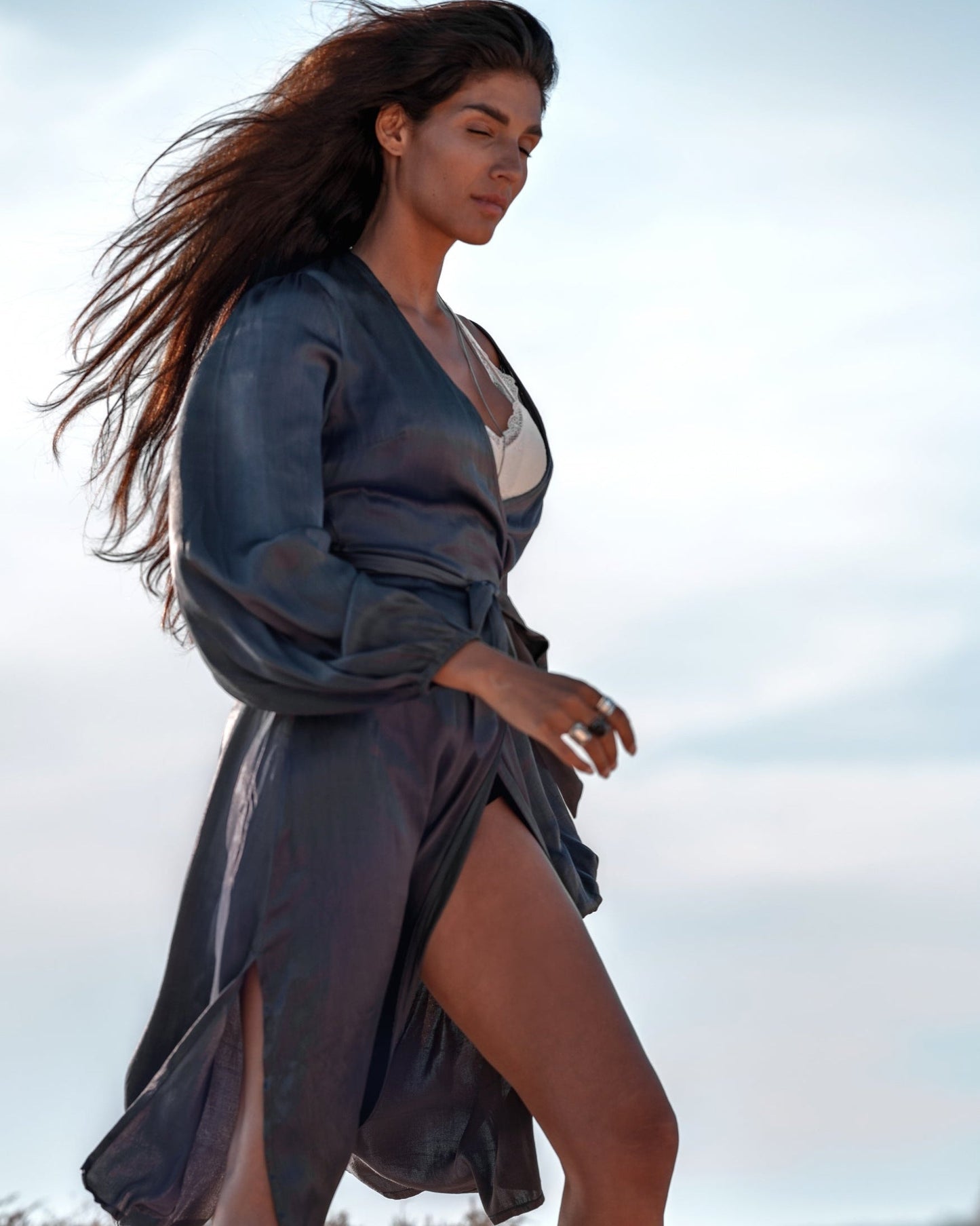 Frau in elegantem, fließendem Kleid spaziert bei Tageslicht. Wind weht durch ihr langes Haar. Mode, Stil, Outdoor-Fotografie.