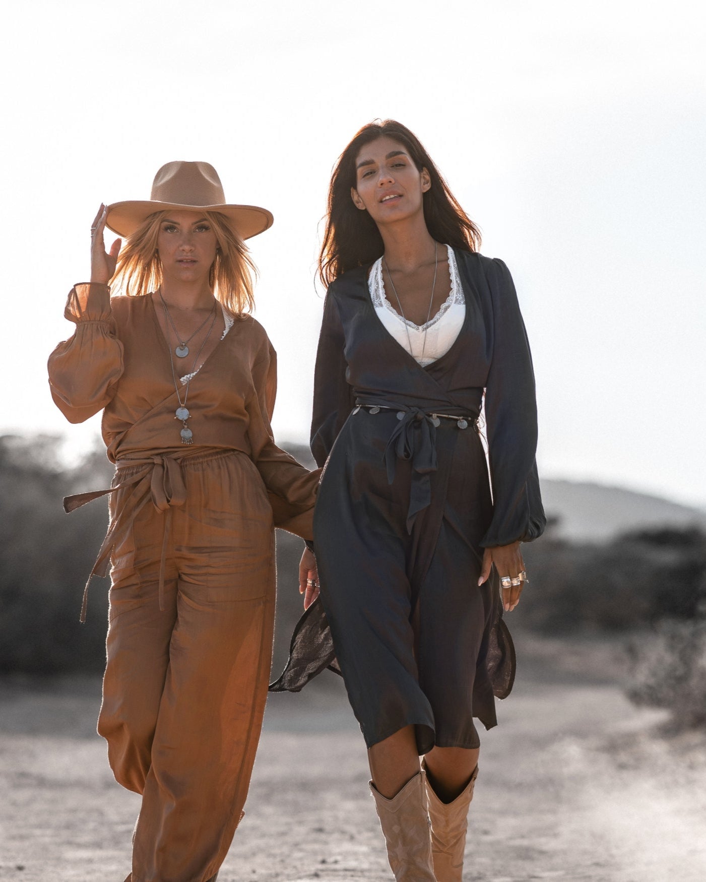 Zwei Frauen in modischen Kleidern und Hüten spazieren in der Natur. Stilvolle Damenmode, Sommeroutfits, Outdoor-Fotografie.