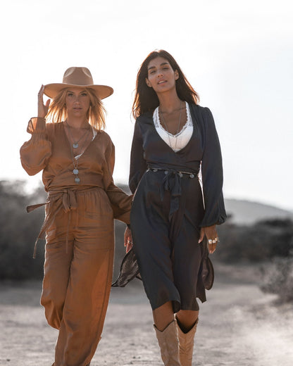 Zwei Frauen in modischen Kleidern und Hüten spazieren in der Natur. Stilvolle Damenmode, Sommeroutfits, Outdoor-Fotografie.
