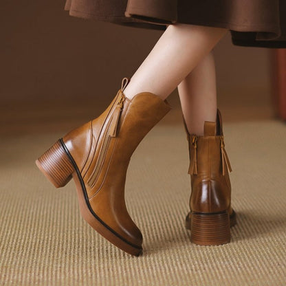 Braune Lederstiefeletten mit Blockabsatz und Reißverschluss, getragen von einer Person auf Teppichboden. Modische Damenstiefel, Herbstmode.