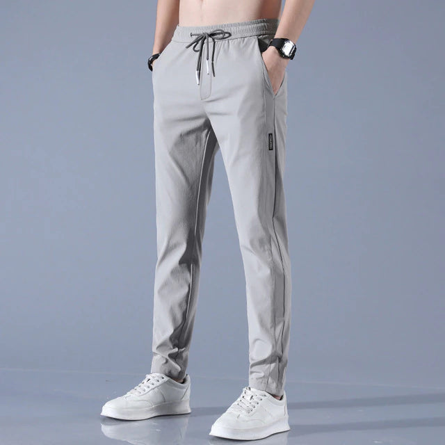 Graue Jogginghose für Herren, modern geschnitten, mit Kordelzug und Taschen, kombiniert mit weißen Sneakers. Ideal für Freizeit und Sport.