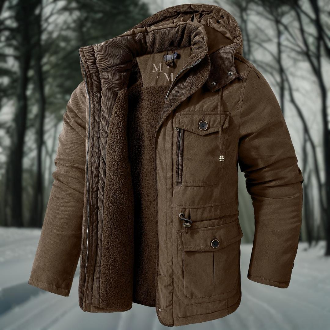 Braune Winterjacke mit Kapuze und Fleece-Innenfutter, ideal für kalte Temperaturen, vor einem verschneiten Waldhintergrund. Perfekt für Outdoor-Aktivitäten.