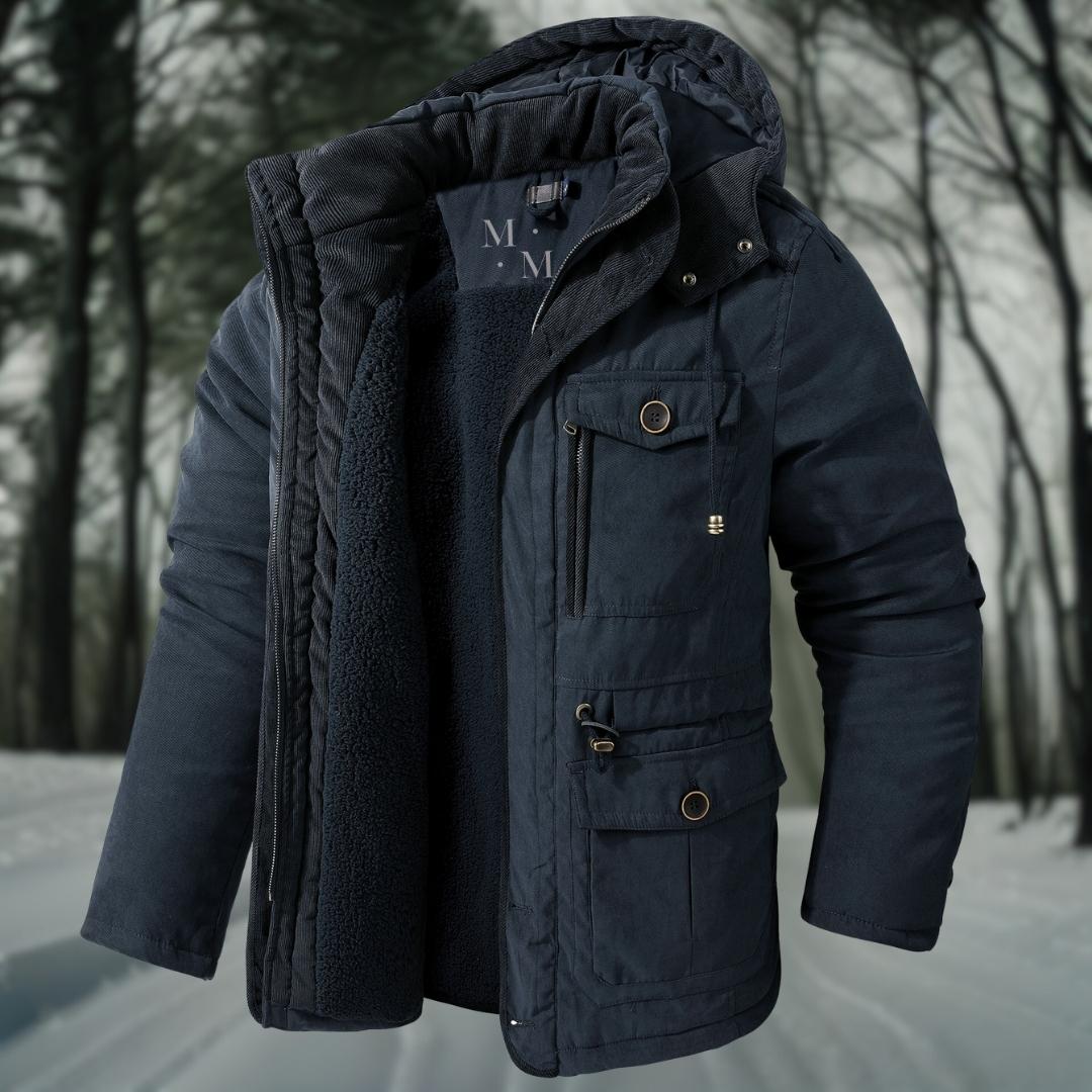 Dunkelblaue Winterjacke mit Kapuze und mehreren Taschen, isoliert vor einem verschneiten Waldhintergrund. Warme Herrenjacke für kalte Temperaturen.