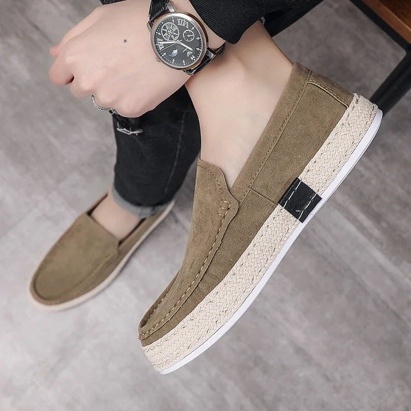 Beige Herren-Slipper aus Wildleder mit geflochtener Sohle, getragen von einer Person mit schwarzer Uhr und Jeans. Elegante Freizeitschuhe für Männer.