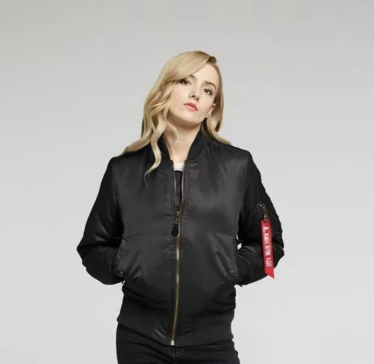 Blonde Frau in schwarzer Bomberjacke mit rotem Etikett, neutraler Hintergrund. Modetrend, Damenbekleidung, lässiger Stil, Herbstmode.