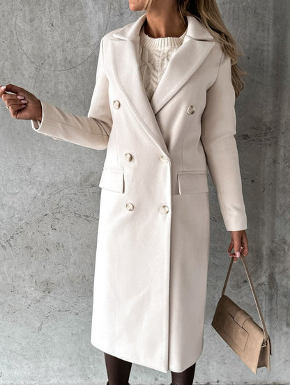Eleganter cremefarbener Damen-Wollmantel, doppelreihig, mit Taschen und Knöpfen, kombiniert mit beiger Handtasche vor grauem Hintergrund.