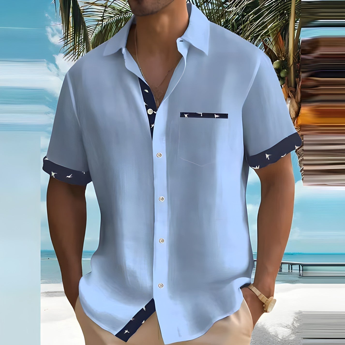 Mann in hellblauem Kurzarmhemd mit Vogelmuster, steht am Strand vor Palmen. Sommermode, Freizeitkleidung, tropische Kulisse.