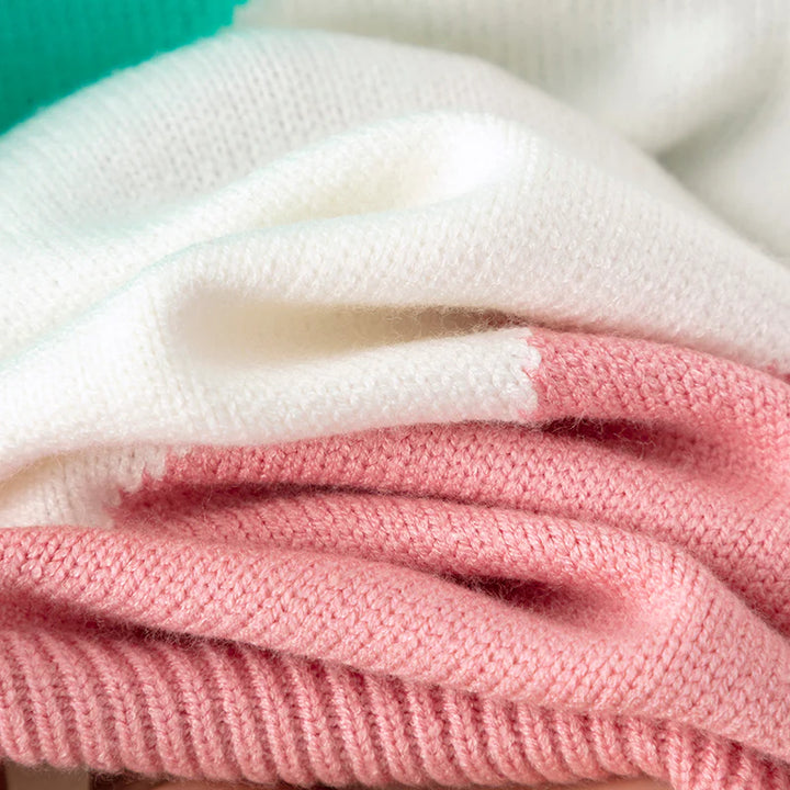 Nahaufnahme von gefalteten Strickpullovern in Weiß, Rosa und Grün. Weiche, hochwertige Wolle, ideal für modische Winterbekleidung.