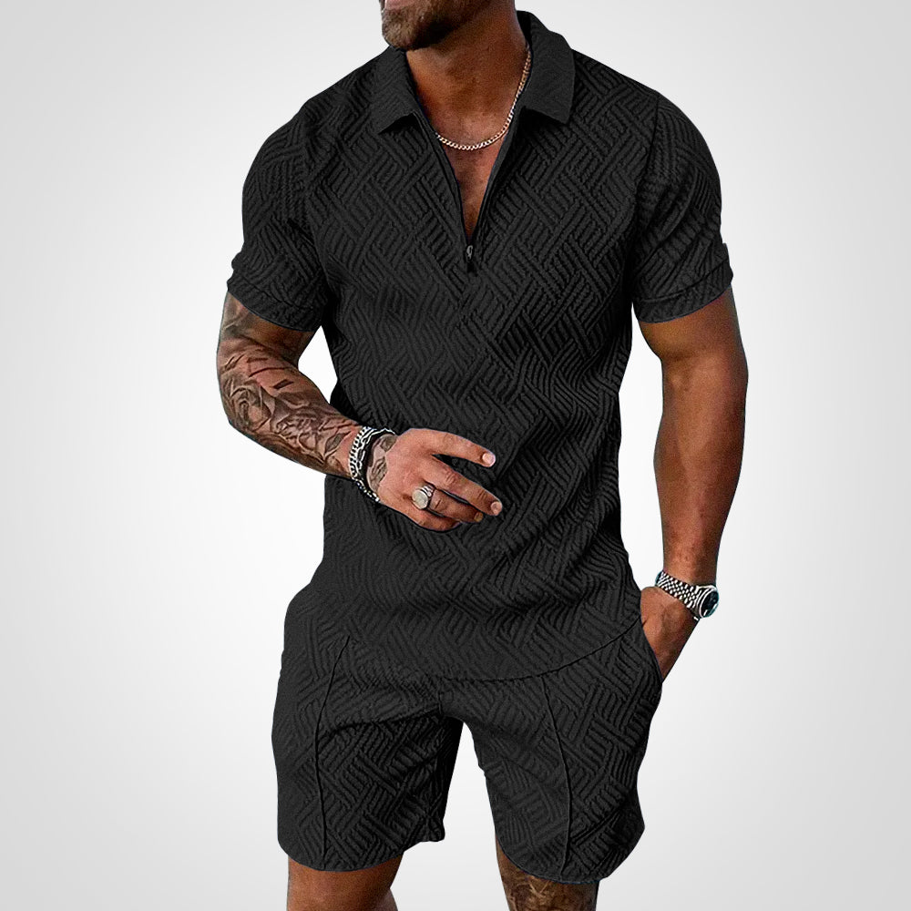 Mann in schwarzem, gemustertem Kurzarm-Poloshirt und Shorts, tätowierter Arm, silberne Kette und Armbanduhr, modischer Sommerlook.