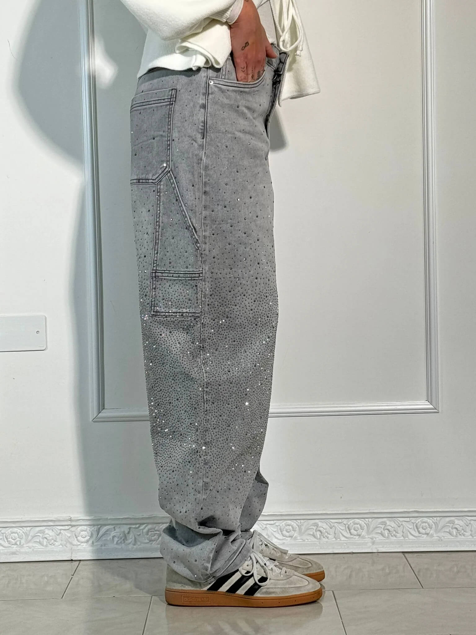 Graue Jeans mit Strasssteinen, seitlicher Tasche und weißen Adidas-Sneakern. Modetrend, Streetwear, Herrenmode, lässiger Stil.