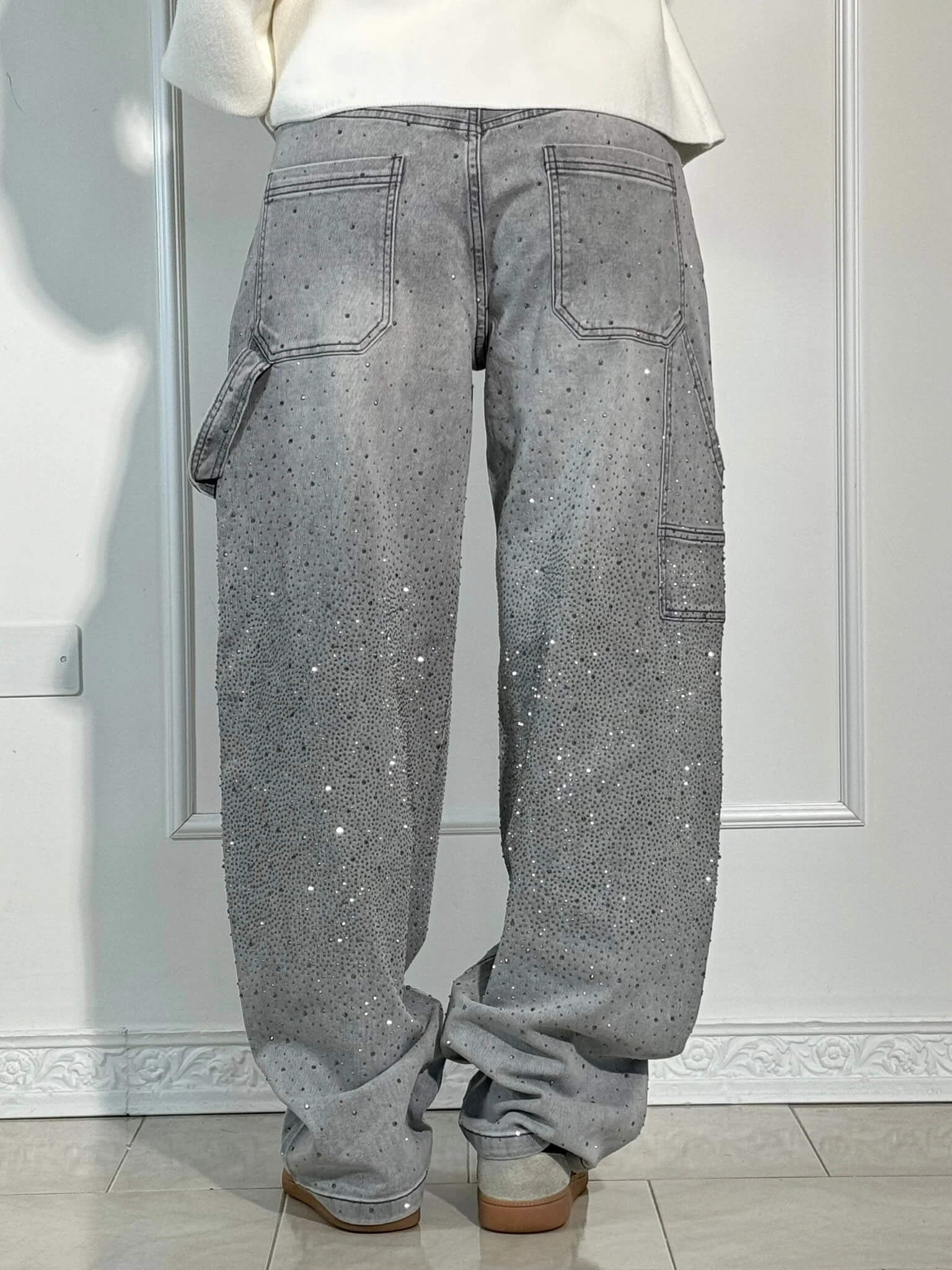 Graue Baggy-Jeans mit Strasssteinen, Rückansicht. Modetrend, lässiger Stil, funkelnde Details. Perfekt für urbanen Look und Streetwear.
