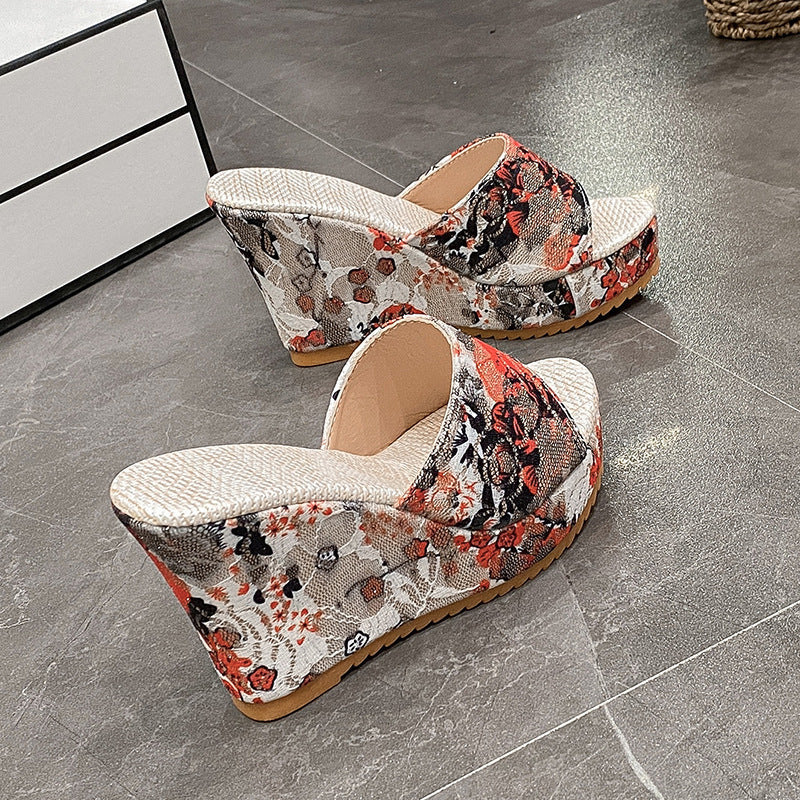 Bunte Keilsandalen mit Blumenmuster auf grauem Boden. Modische Sommerschuhe, Damenmode, bequeme Plateau-Sandalen, trendige Fußbekleidung.