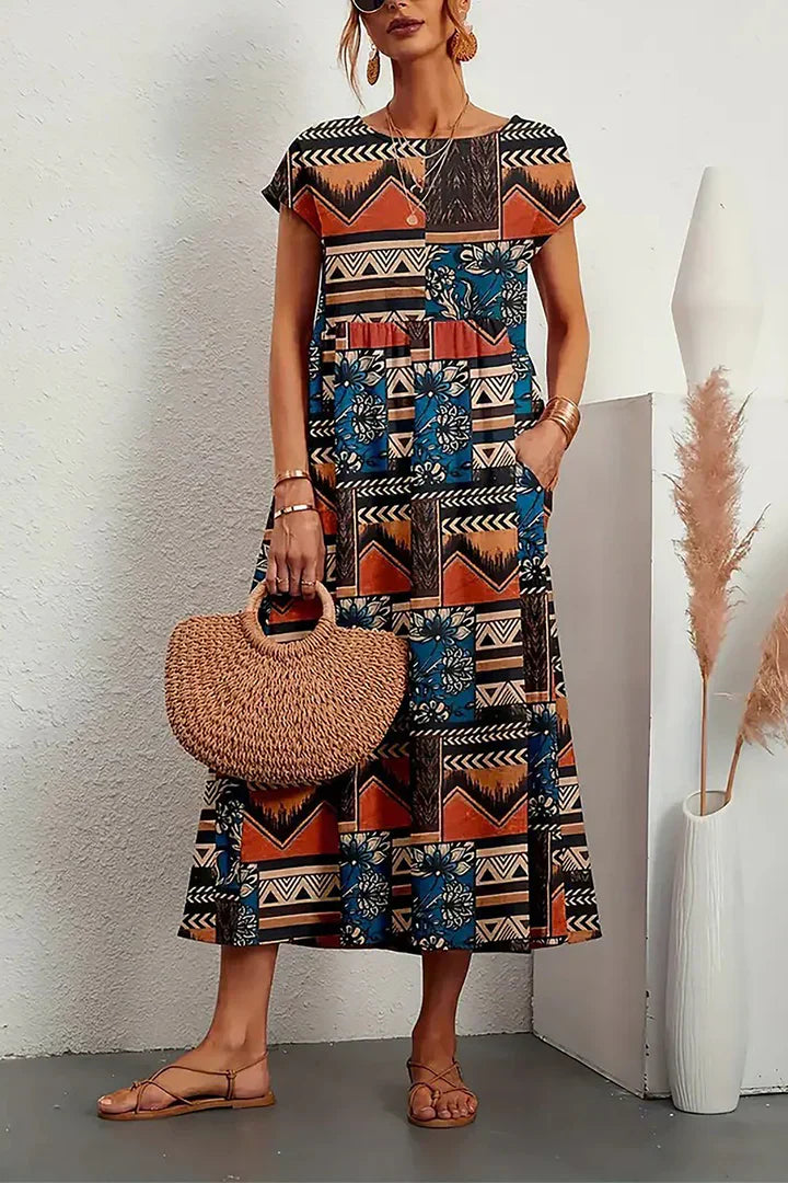 Frau in buntem, geometrisch gemustertem Maxikleid mit Strohtasche und Sandalen, steht vor weißer Wand. Boho-Chic, Sommermode, lässiger Stil.