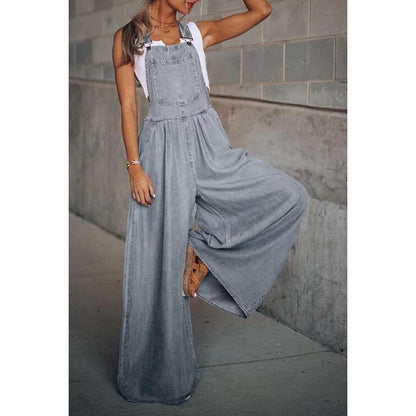 Frau in grauem, weitem Jeans-Overall vor Betonwand, modisch und lässig, Streetwear-Trend, Sommermode, stilvolle Damenbekleidung.