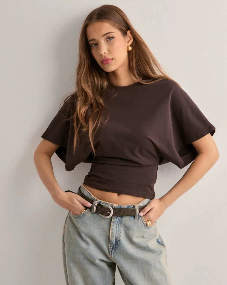 Junge Frau in braunem T-Shirt und Jeans posiert vor weißer Wand. Modetrend, lässiger Stil, Damenbekleidung, Freizeitlook.