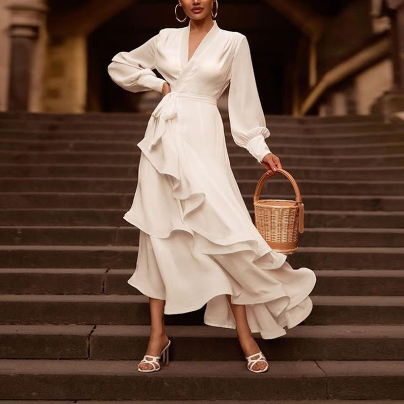 Frau in elegantem weißen Wickelkleid mit Rüschen, hält einen runden Korb auf Treppe. Modetrend, stilvolle Abendgarderobe, Sommermode.
