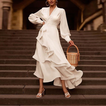 Frau in elegantem weißen Wickelkleid mit Rüschen, hält einen runden Korb auf Treppe. Modetrend, stilvolle Abendgarderobe, Sommermode.