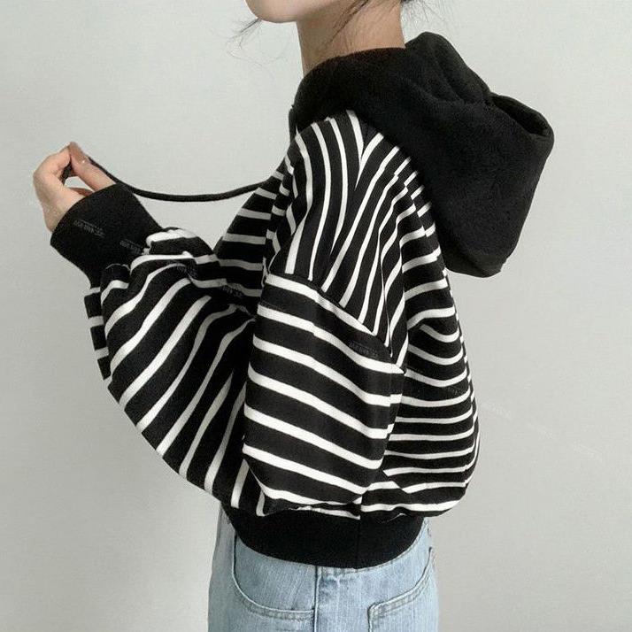 Frau in gestreiftem schwarz-weißem Hoodie, seitlich, mit Kapuze und blauen Jeans. Modetrend, lässiger Stil, Streetwear.