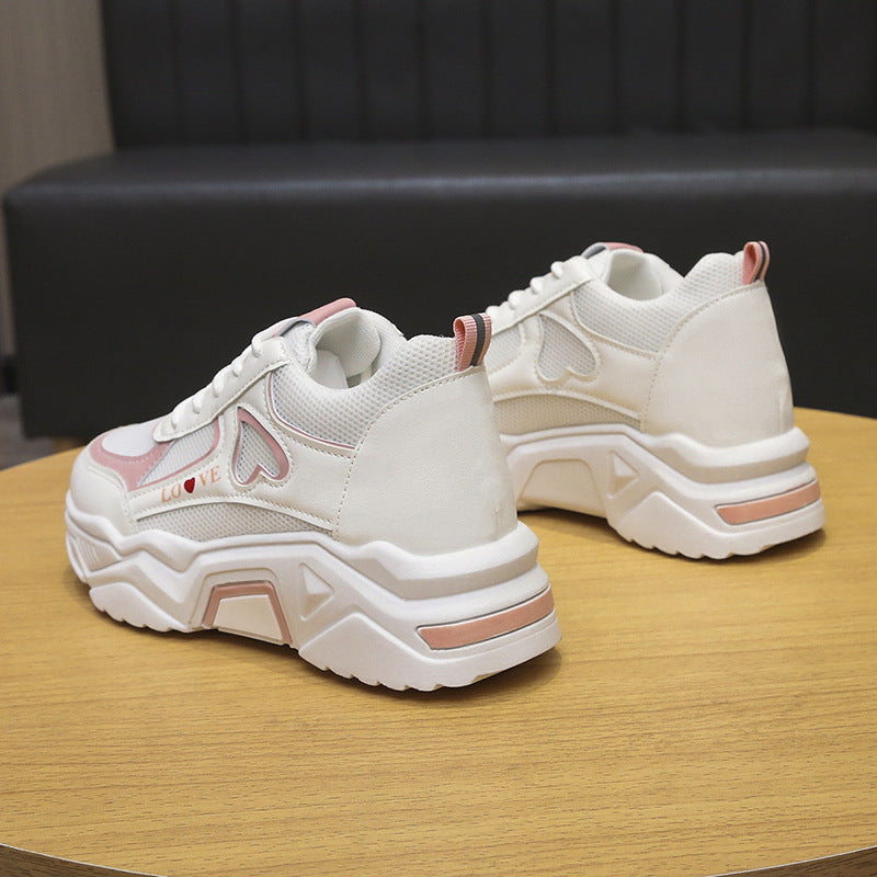 Weiße Damen-Sneaker mit rosa Akzenten und Herzdesign auf Holztisch. Modische Plateau-Schuhe, ideal für trendbewusste Frauen.