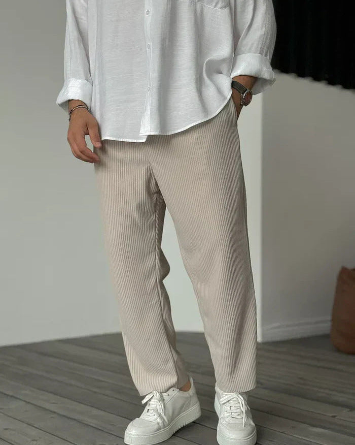 Weiße Hemdbluse und beige, gerippte Hose kombiniert mit weißen Sneakern auf Holzboden. Modetrend, lässiger Stil, Herrenmode, minimalistisch.