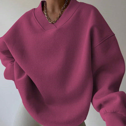 Frau trägt oversized magenta Pullover mit V-Ausschnitt und goldener Kette. Modetrend, lässiger Stil, Herbstmode, Damenbekleidung.