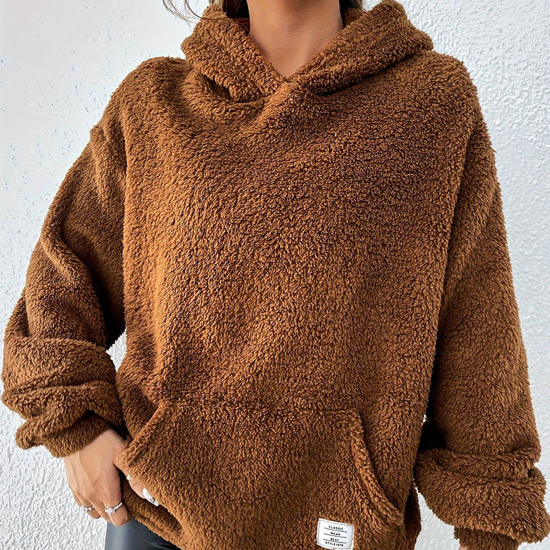 Frau in braunem Teddy-Fleece-Hoodie vor weißer Wand. Kuscheliger Pullover, modisch, warm, ideal für Herbst und Winter.