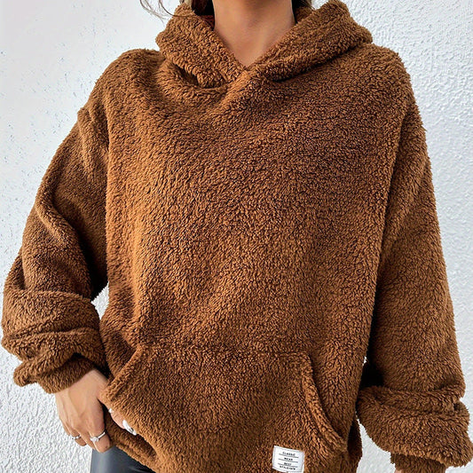 Frau in braunem Teddy-Fleece-Hoodie vor weißer Wand. Kuscheliger Pullover, modisch, warm, ideal für Herbst und Winter.