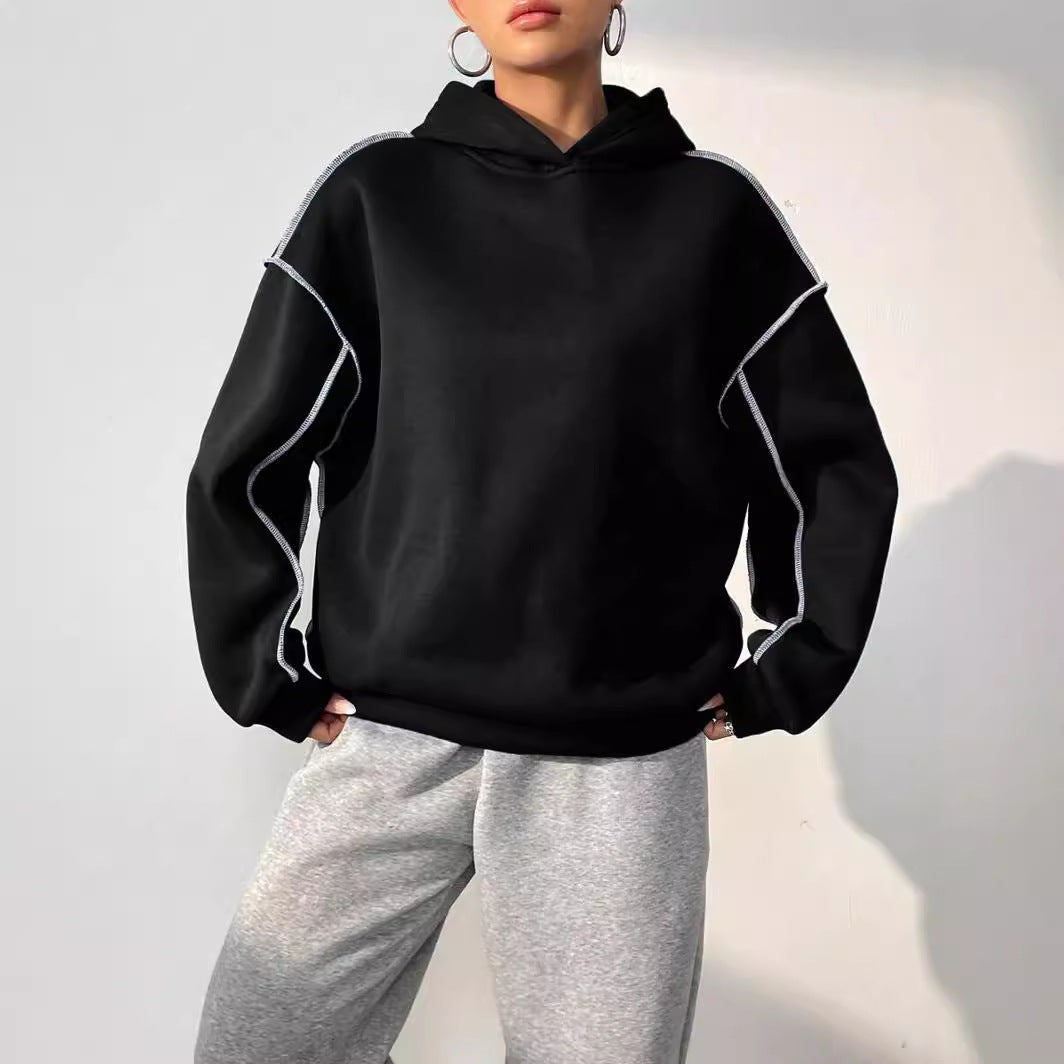 Schwarzer Oversize-Hoodie mit weißen Nähten, kombiniert mit grauer Jogginghose. Modetrend, lässiger Streetwear-Look, bequeme Freizeitkleidung.