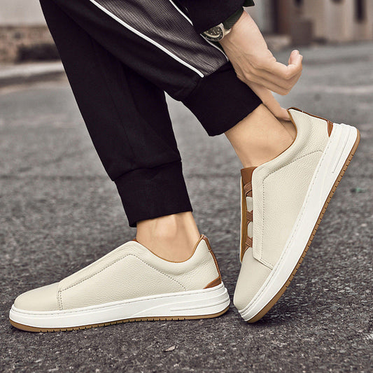 Beige Herren-Sneaker aus Leder, rutschfeste Sohle, lässiger Stil, getragen von Person in schwarzer Hose auf Asphaltstraße.