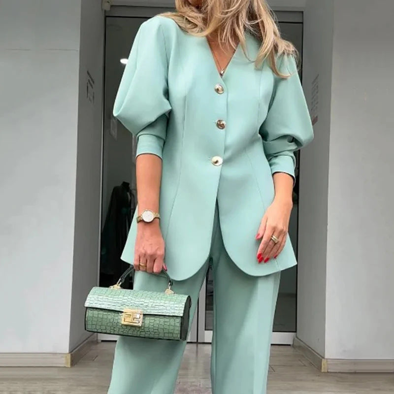 Frau in mintgrünem Hosenanzug mit Puffärmeln, goldenen Knöpfen und passender Handtasche. Elegante Mode, Business-Outfit, stilvoller Look.