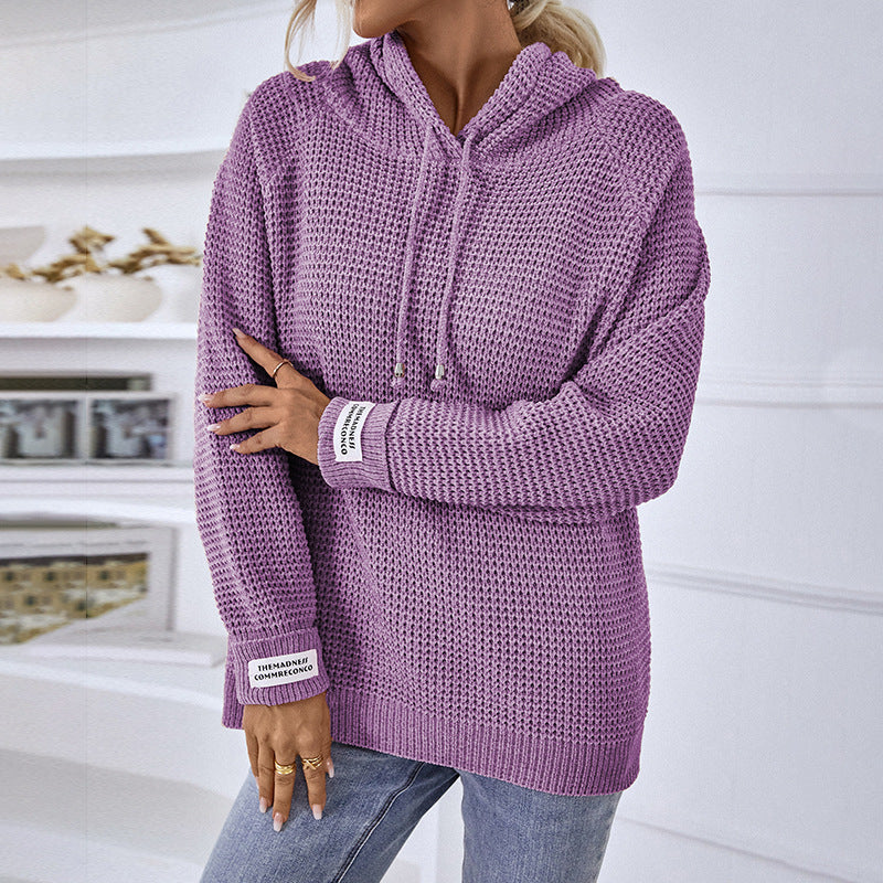 Frau in lila Strickpullover mit Kapuze, lässig und modisch, steht in modernem Raum. Perfekt für Herbstmode und gemütliche Outfits.