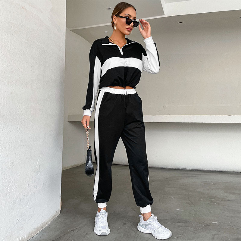 Frau in schwarz-weißem Trainingsanzug mit Sonnenbrille und Handtasche, steht in modernem Raum. Sportliche Mode, Freizeitkleidung, Streetwear-Trend.