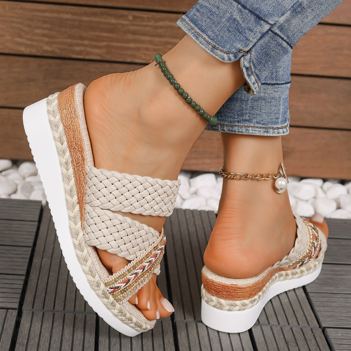 Damenfüße in geflochtenen Sandalen mit Keilabsatz, Jeans, grünem und goldfarbenem Fußkettchen. Sommermode, bequeme Schuhe, Outdoor.