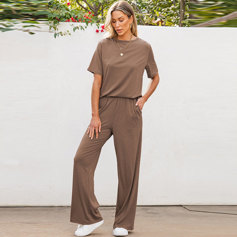 Frau in braunem Freizeitanzug, bestehend aus T-Shirt und Hose, steht vor weißer Wand. Lässige Mode, bequeme Damenbekleidung, Sommeroutfit.