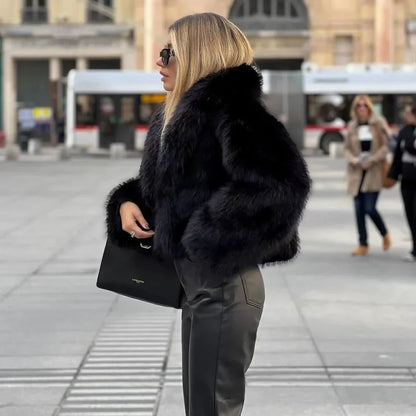 Frau in schwarzer Pelzjacke und Lederhose, hält eine schwarze Handtasche, steht auf städtischem Platz. Elegante Wintermode, stilvolle Accessoires.