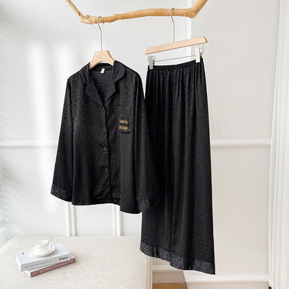 Schwarzer Satin-Pyjama-Set mit Leopardenmuster, bestehend aus Hemd und Hose, auf Holzkleiderbügel. Elegante Nachtwäsche für Damen.
