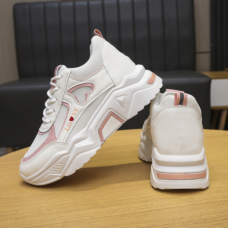 Weiße und rosa Damen-Sneaker mit Herzmotiv, dicker Sohle und modernem Design auf Holztisch. Modische Sportschuhe für Damen.