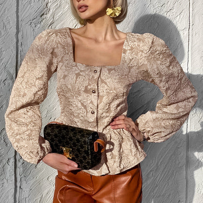 Frau in beiger Spitzenbluse mit Puffärmeln, brauner Lederhose und schwarzer Designerhandtasche vor grauer Wand. Fashion, Damenmode, Streetstyle.